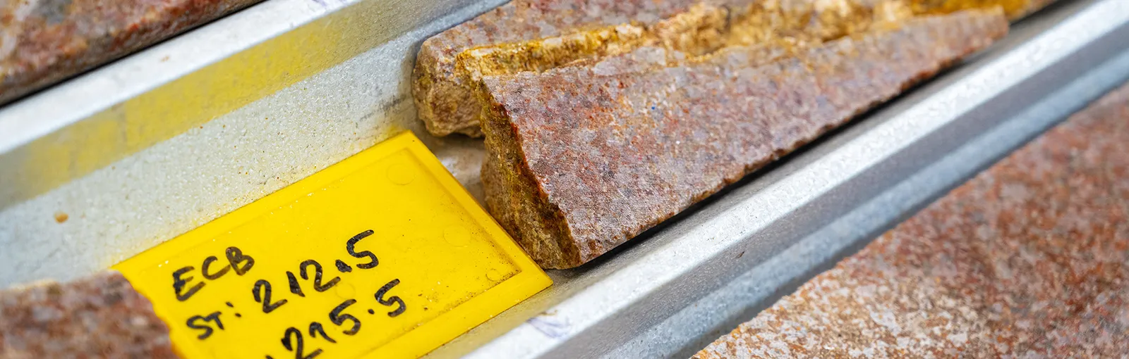 Close-up of labelled rock core samples from lithium exploration drilling, stored in metal trays for geological analysis.