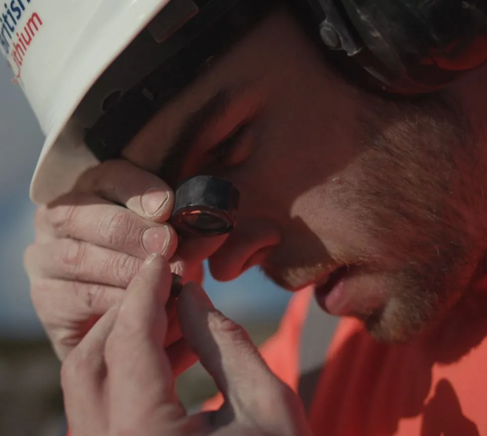 British Lithium geologist inspecting mineral sample with hand lens during field analysis in Cornwall exploration site.