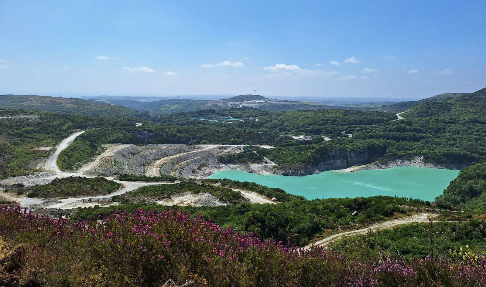 Imerys British Lithium Cornwall UK quarry with turquoise lake, green hills, winding paths and countryside under blue sky