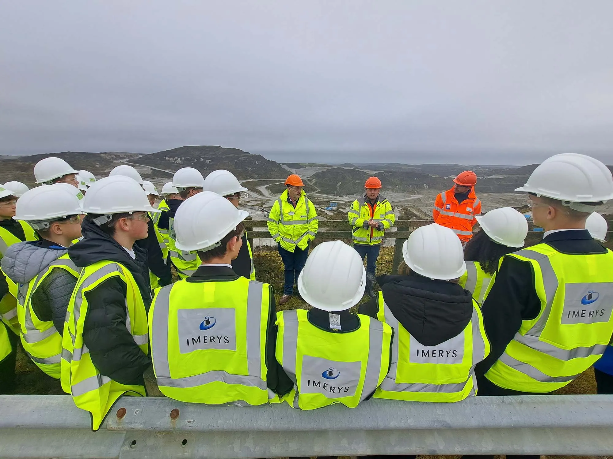 Students and workers in safety helmets and high-visibility jackets with Imerys logo during an educational quarry site visit