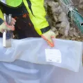 Geological sampling bag labeled with ID tickets being sealed at British Lithium exploration site for traceability and analysis.