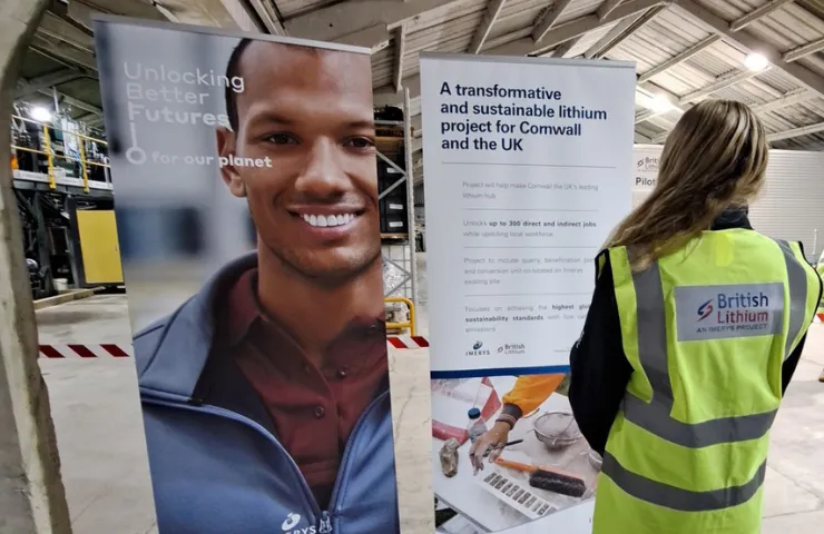 Person in British Lithium vest viewing display banners about sustainable lithium project and job creation in Cornwall industrial facility.